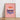 "This is our happy place" pink poster by Almanac Co Prints framed on a wooden floor against a white wall.